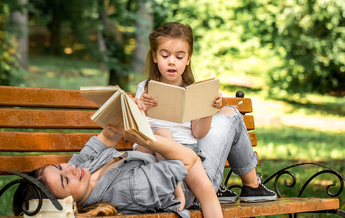 Mother And daughter reading books on a park bench